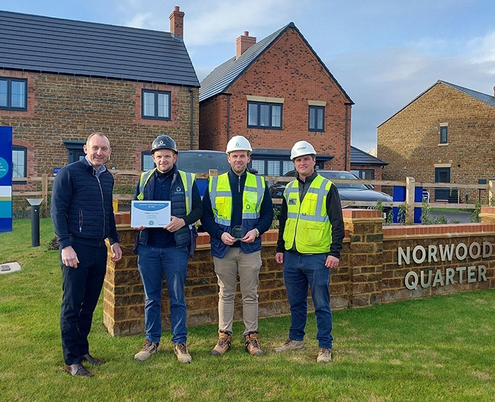 Three carpenters in LJ Construction branded PPE accepting award from Miller Homes representative for excellent performance on the Norwood Quarter development