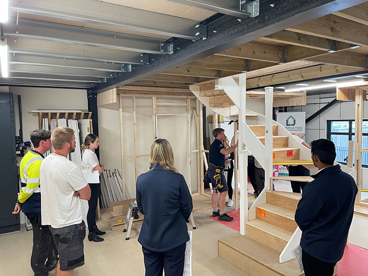 Group gathered round watching construction of staircase at LJ Construction carpentry academy workshop