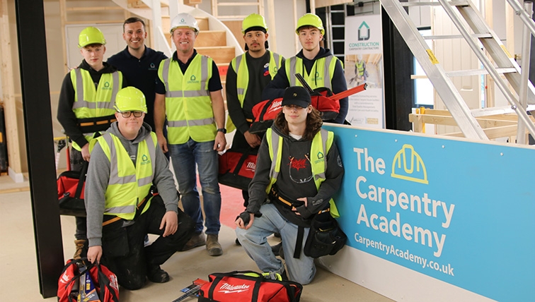 Trainee carpenters with LJ construction funded starter tool bags in front of Carpentry Academy Signage